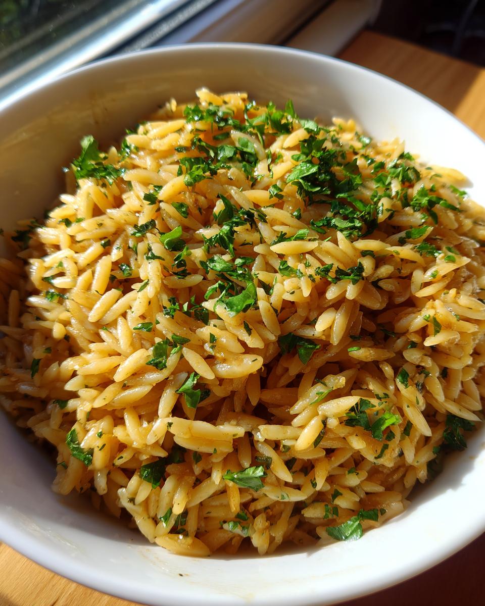 Close-up of fluffy rice pilaf made with orzo pasta, glistening and topped with fresh chopped parsley.