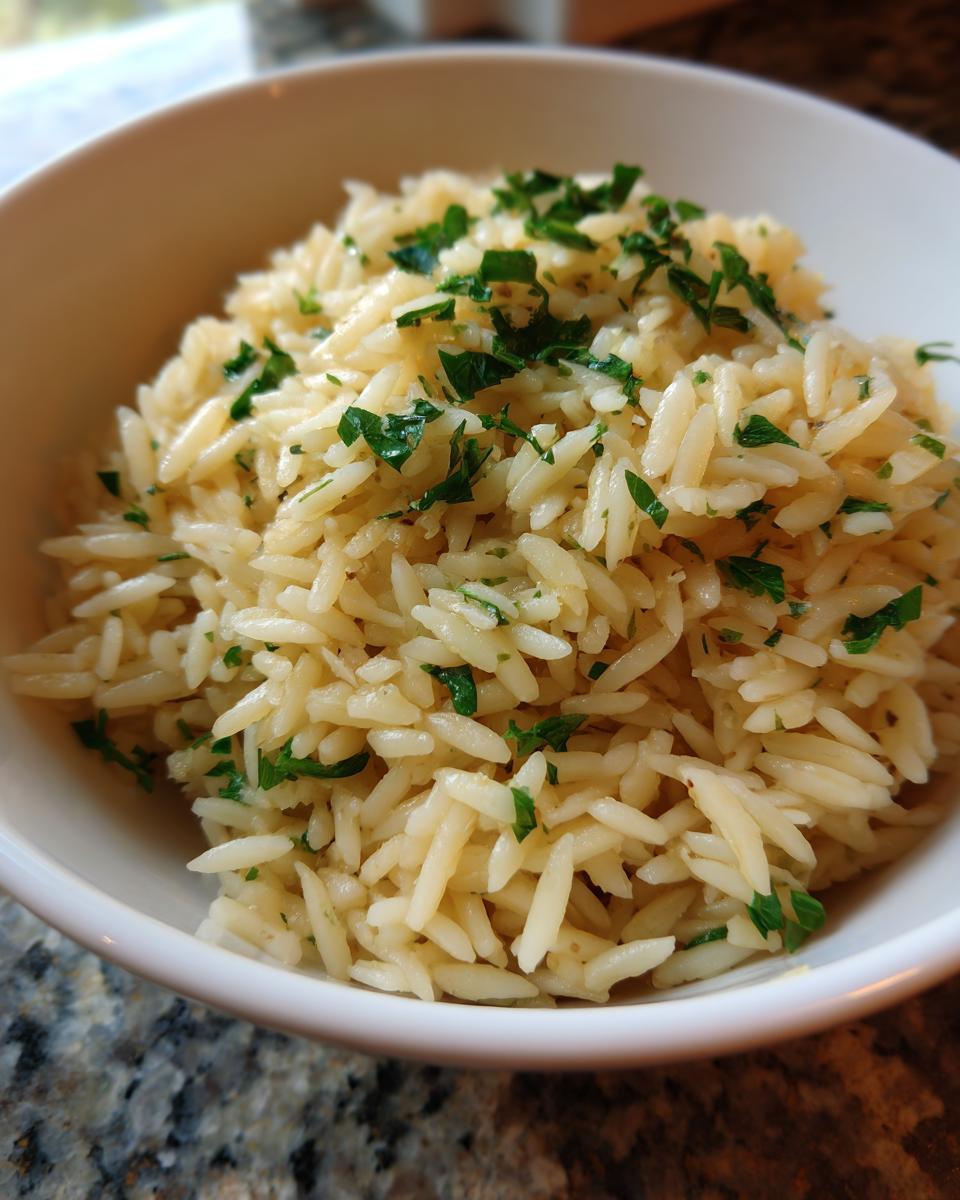 Close-up of fluffy rice pilaf made with orzo pasta, served in a white bowl and garnished with chopped green parsley.