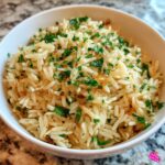 Close-up of fluffy rice pilaf, lightly browned with visible orzo pasta pieces, topped generously with chopped fresh parsley.