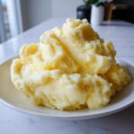 A generous serving of fluffy, creamy slow cooker mashed potatoes topped with melted butter on a white plate.