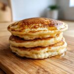 A tall stack of three fluffy sourdough discard pancakes drizzled with syrup on a wooden board.