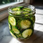 Close-up of sliced cucumbers soaking in brine with fresh dill and peppercorns for refrigerator pickles.