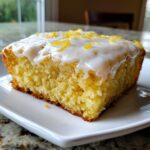 A close-up of a square slice of fudgy lemon brownies topped with white glaze and bright yellow lemon zest.