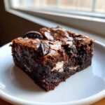 Close-up of a fudgy Oreo brownie slice topped with whole Oreo pieces, showing a shiny crust.