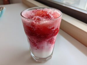 A tall glass showing layers of white milk and bright red, frothy strawberry mixture, creating homemade strawberry milk.