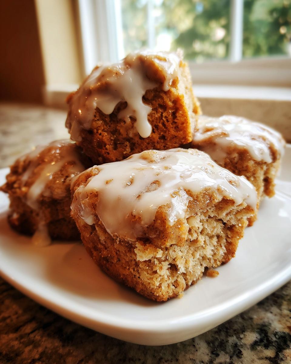 Close-up of four squares of baked apple fritters topped with thick white glaze, served on a white dish.