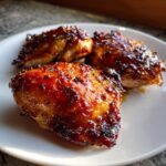 Three pieces of perfectly glazed, crispy baked chicken thighs served on a white plate.