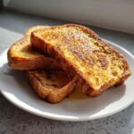 Three golden-brown slices of easy french toast stacked on a white plate, glistening with syrup.