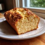 A golden-brown loaf of quick soda bread, sliced to show its soft crumb, resting on a white plate.