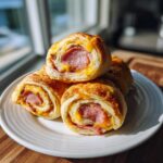A stack of four golden-brown sausage pinwheels filled with sausage and melted cheddar cheese, served on a white plate.