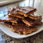 A stack of broken pieces of graham cracker toffee topped with melted chocolate and sprinkled with sea salt.