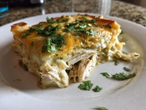 A thick slice of green chile chicken enchiladas casserole topped with melted cheese and fresh cilantro.