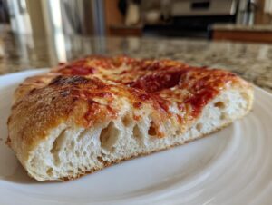 Close-up of a thick slice of homemade pizza showing the airy, bubbly cross-section of the crust and melted cheese.