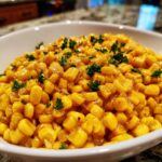 Close-up of bright yellow honey butter corn kernels garnished with fresh parsley in a white bowl.