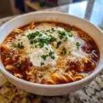 A close-up of a hearty bowl of instant pot lasagna soup topped with dollops of ricotta, shredded mozzarella, and fresh parsley.
