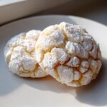 Close-up of two delicious lemon crinkle cookies heavily dusted with powdered sugar on a white plate.