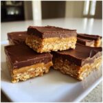 A stack of rich lunch lady peanut butter bars featuring an oat base, peanut butter layer, and chocolate topping.