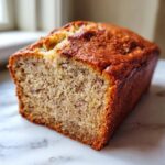 Close-up of a freshly baked, moist loaf of banana bread recipe showing its golden crust and speckled interior.