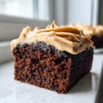 Close-up of a dark, moist slice of gingerbread cake topped with swirled brown sugar frosting.