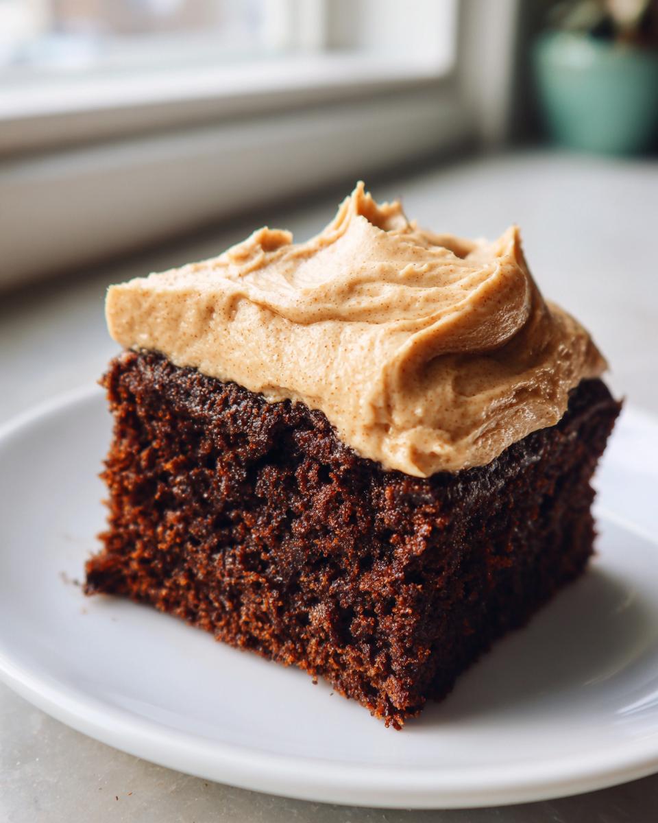 Close-up of a moist, dark slice of gingerbread cake topped with a swirl of light brown spice frosting.