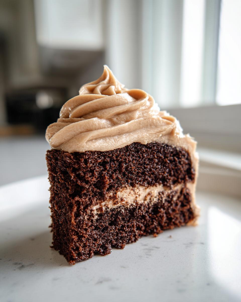 A close-up of a rich, dark slice of moist gingerbread cake with a layer of filling and a swirl of light brown frosting.