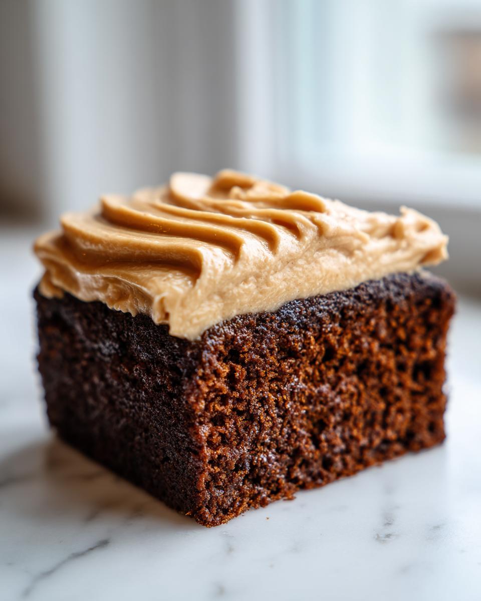 A close-up of a moist, dark slice of gingerbread cake topped with swirled brown sugar or caramel frosting.