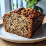 A close-up of a freshly baked loaf of greek yogurt banana bread studded with chocolate chips, resting on a plate.