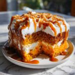 A slice of moist pumpkin poke cake layered with cream and drizzled heavily with caramel sauce.