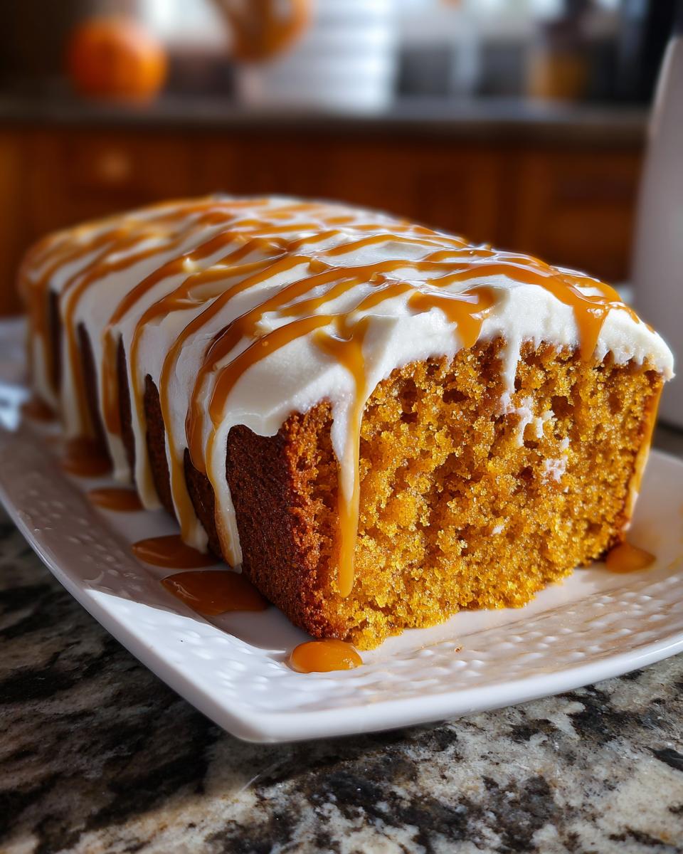 A close-up of a slice of moist pumpkin poke cake topped with white frosting and drizzled with caramel sauce.