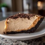 A close-up slice of no bake peanut butter pie featuring a thick, creamy filling and dark chocolate crust, topped with crumbs.