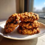 A stack of four textured, golden-brown breakfast cookie fuel rounds containing visible raisins on a white plate.