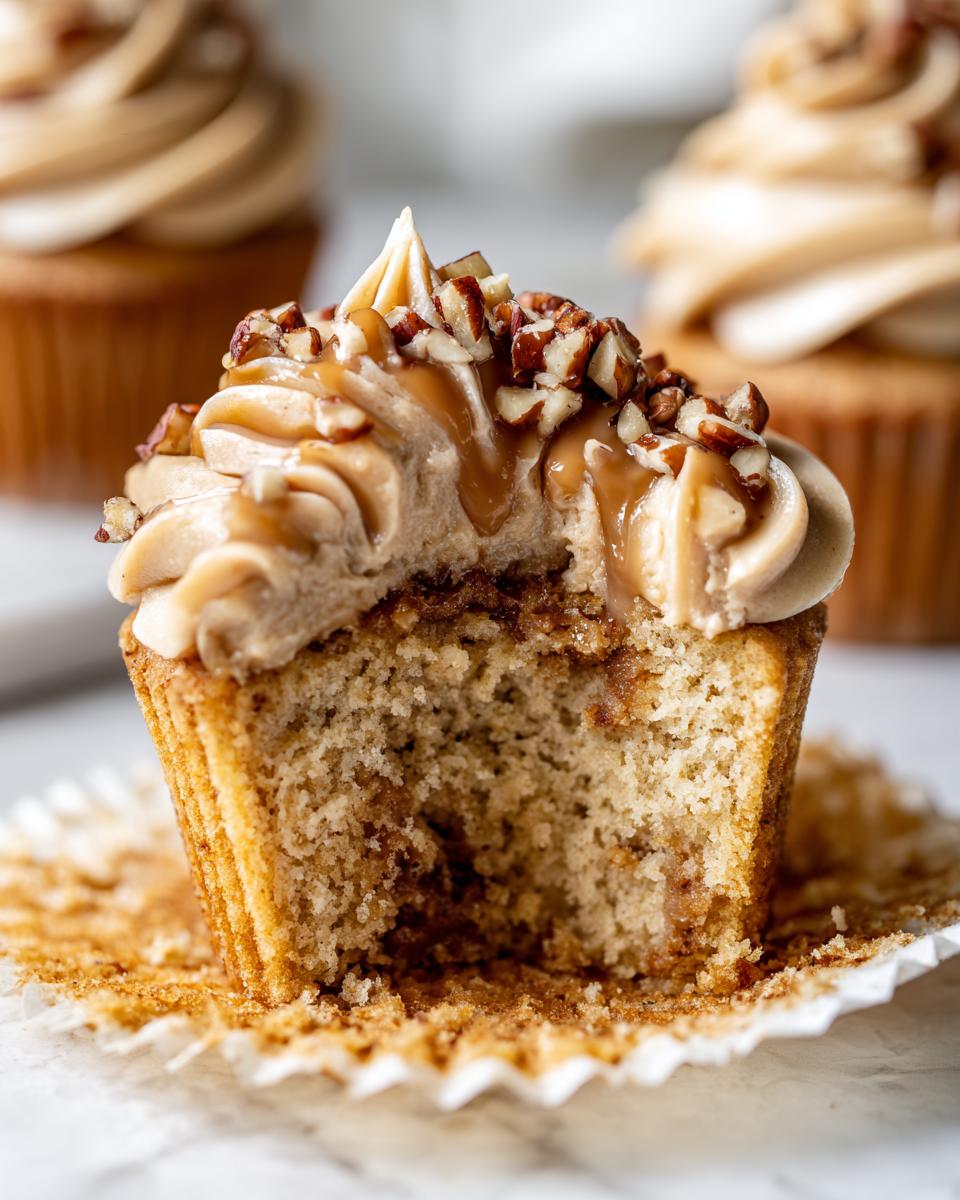 Close-up of a pecan pie cupcakes with a bite taken out, showing moist cake, caramel frosting, and chopped pecans.