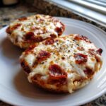 Close-up of two perfectly melted pepperoni english muffin pizza halves on a white plate, sprinkled with herbs.