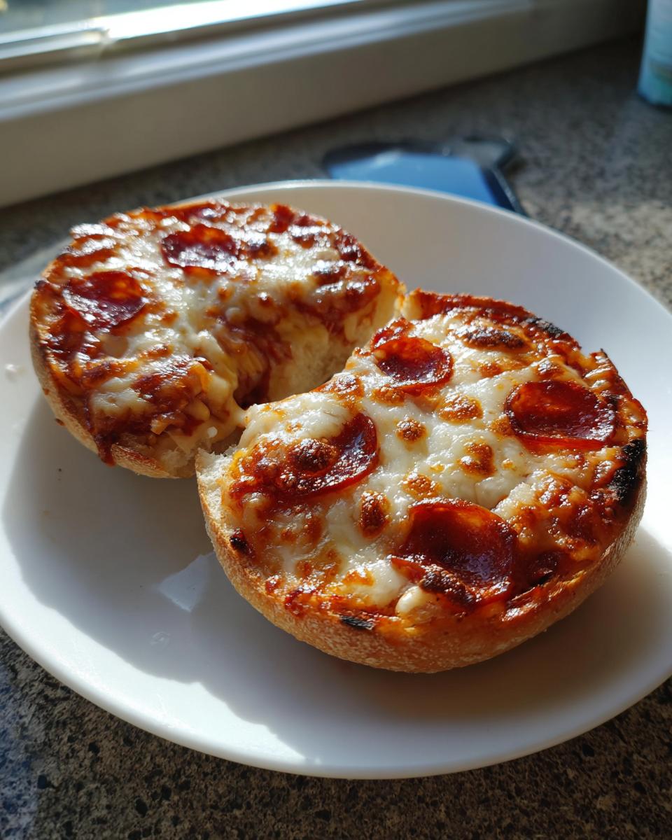Two halves of a freshly baked pepperoni english muffin pizza with melted, bubbly cheese on a white plate.