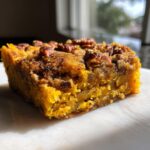A close-up, appetizing slice of bright orange pumpkin crunch cake topped with crunchy pecans.