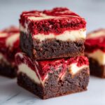 Two stacked, rich chocolate red velvet cheesecake brownies with a marbled red and cream cheese swirl topping.