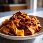 Close-up of wide pappardelle pasta generously coated in rich, slow-cooked bolognese sauce.