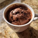 A close-up of rich, airy chocolate mousse topped with shavings, served in a white mug.