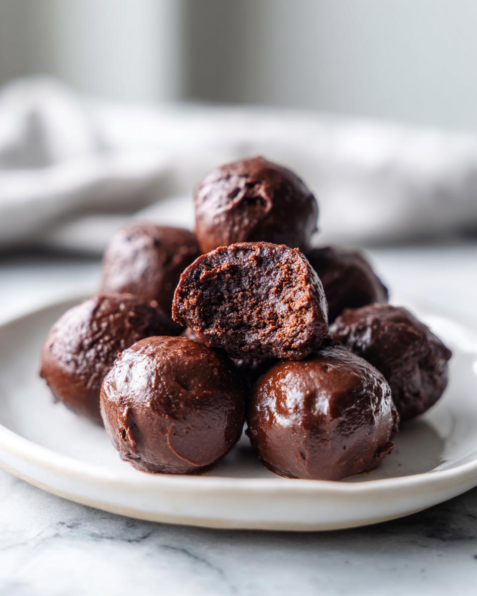 A stack of decadent, chocolate-coated Oreo balls, with one bitten open to show the dark, fudgy interior.