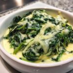 Close-up of rich creamed spinach recipe served in a white bowl, topped with melted white cheese.