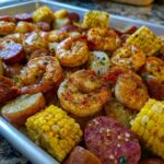 Close-up of seasoned shrimp, corn on the cob, sausage, and potatoes for a sheet pan shrimp boil.