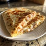 Two golden-brown halves of a cheesy shrimp quesadilla overflowing with pink shrimp and melted cheese.