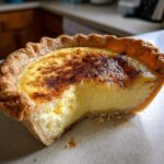 Close-up of a single serving custard pie with a bite taken out, showing the silky filling and browned top.