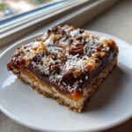 Close-up of a single square of magic cookie bars layered with crust, caramel, chocolate, nuts, and coconut.