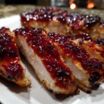 Close-up of sliced cranberry chicken breasts covered in a thick, glossy, dark red cranberry glaze.