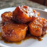 Close-up of four glazed, caramelized slices of southern candied yams sitting in syrup on a white plate.