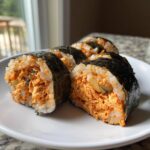 Four slices of homemade tuna kimbap featuring spicy orange tuna filling, served on a white plate.