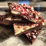 A stack of broken pieces of homemade peppermint bark featuring dark chocolate, white chocolate, and crushed candy canes.
