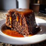 A close-up of a rich, dark portion of sticky toffee pudding generously covered in dripping toffee sauce.