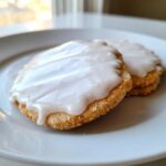 Two round sugar cookies topped with thick, glossy white sugar cookie icing that hardens.